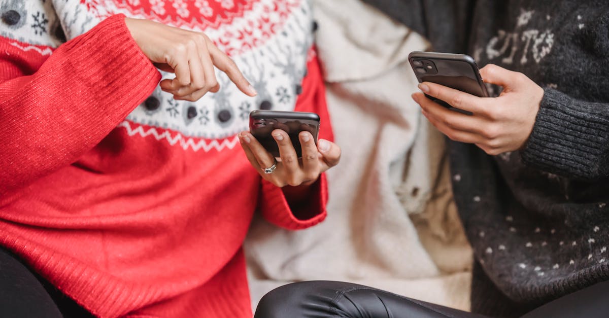 Two women in festive sweaters using smartphones indoors during winter.