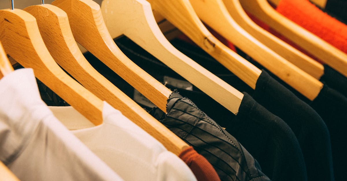 A close-up view of a row of clothes on wooden hangers, showcasing various fabrics and colors in a wardrobe setting.